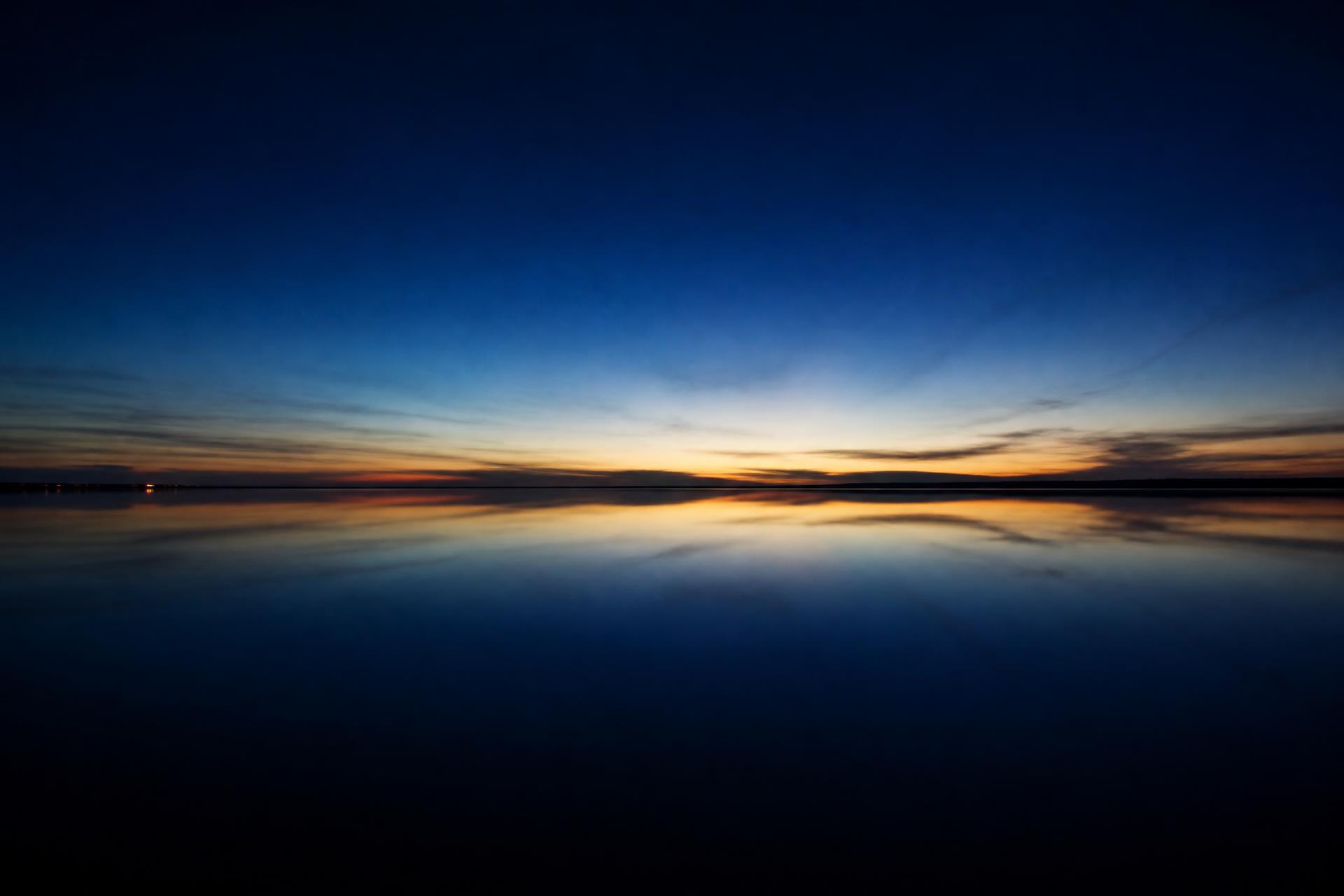 Still water reflecting a faint gold horizon at blue hour