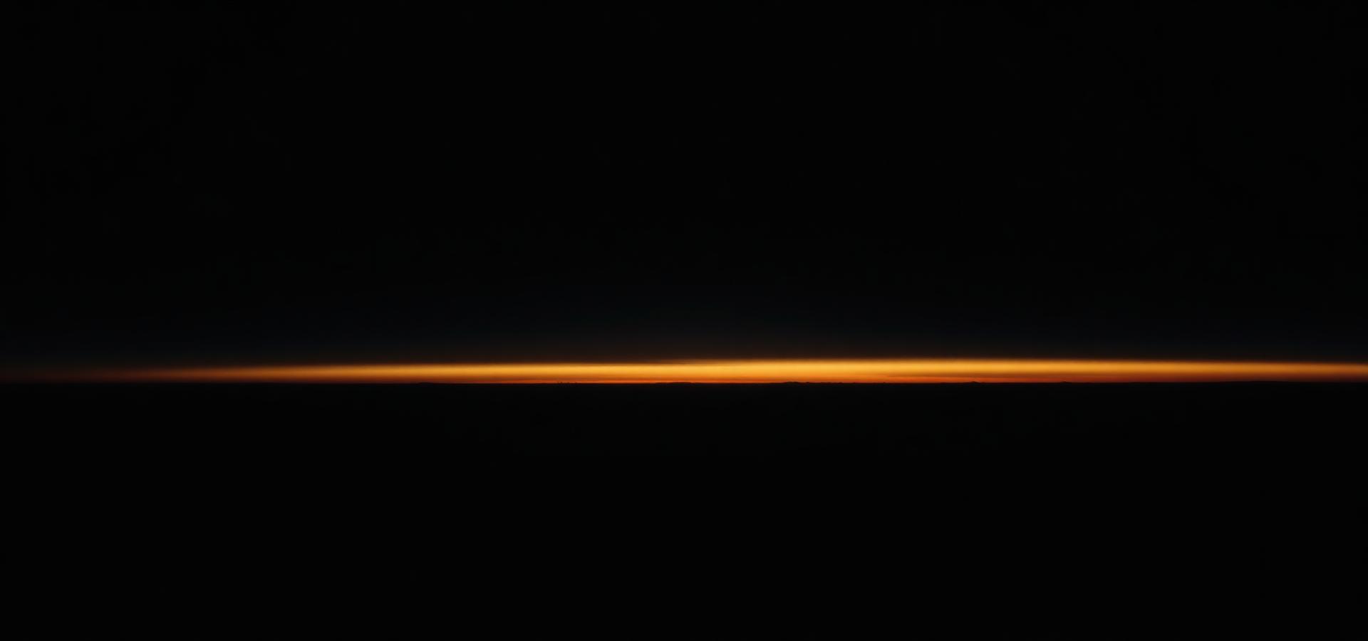 A thin band of gold light along a dark dawn horizon