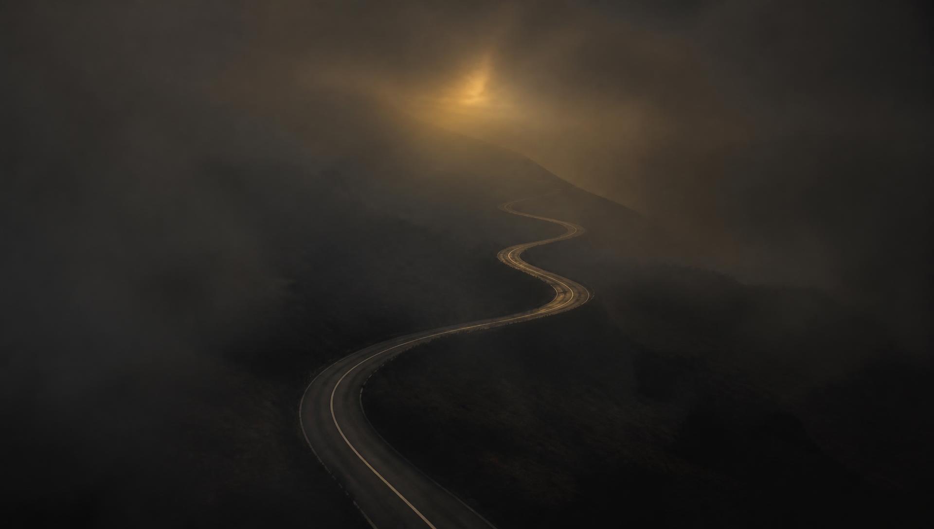 A winding road disappearing into golden fog at dawn