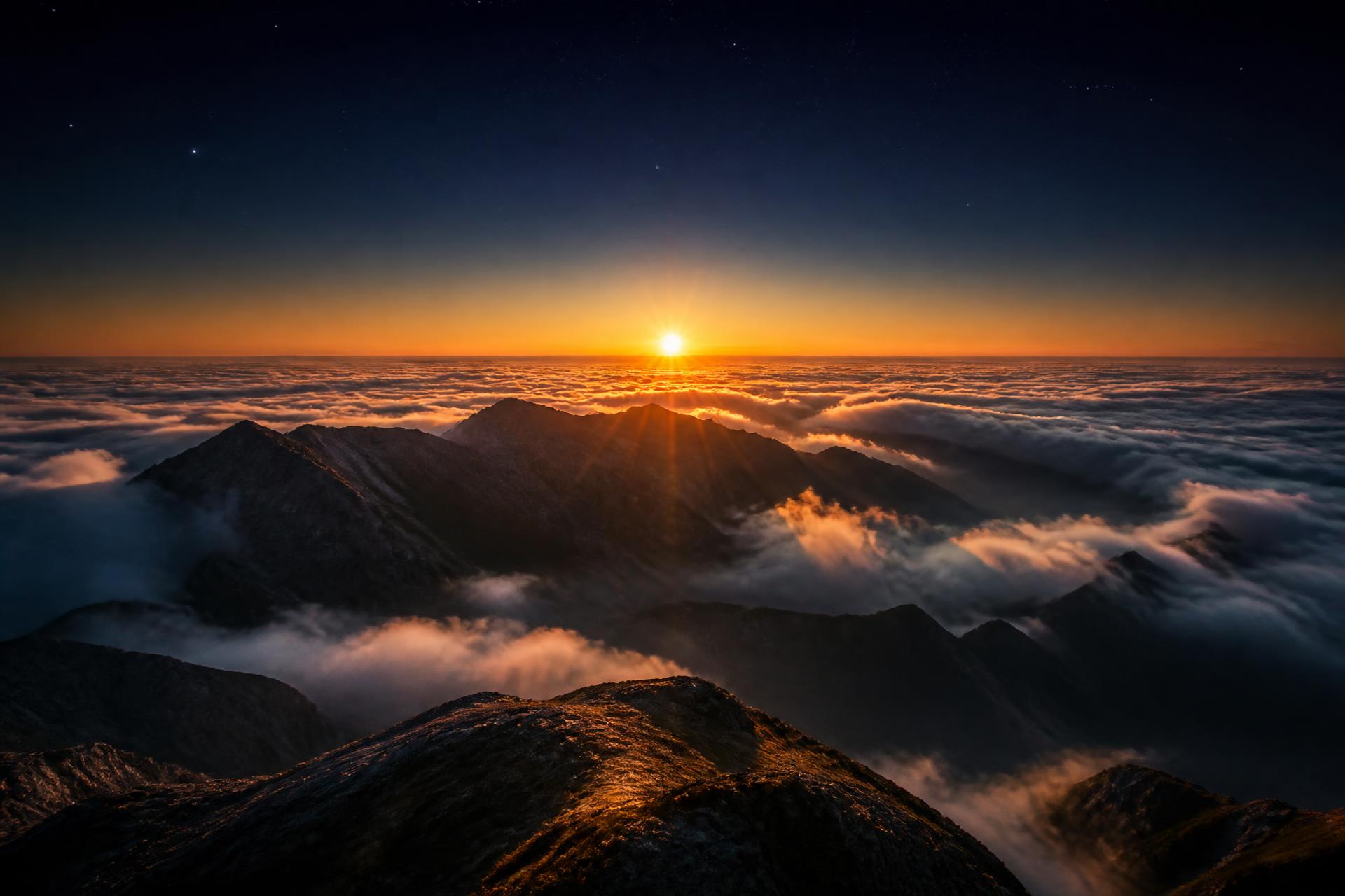 Sunrise breaking over a sea of clouds and dark mountain ridges
